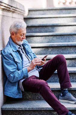 Üst sınıftan bir adam merdivenlerde oturuyor ve telefonda mesajlar yazıyor..