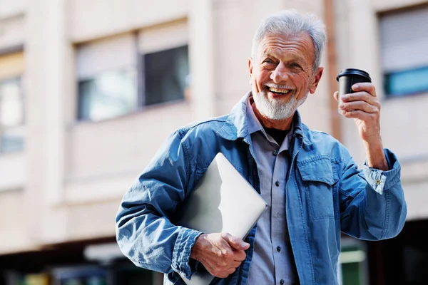 Mutlu bir son sınıf öğrencisi sokakta dizüstü bilgisayarını ve kahve fincanını tutuyor. Son sınıf öğrencisi bir konferansa gidiyor..