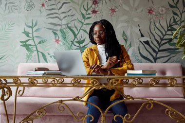 Öğrenci değişim programındaki Afrikalı bir kız öğrenci bir kafede oturuyor ve dizüstü bilgisayarında ödev yazıyor. Öğrenci değişimi.