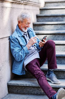Mutlu bir son sınıf öğrencisi merdivenlerde oturmuş telefonda flört ediyor..