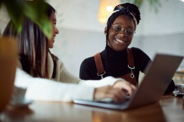 Çok kültürlü kız öğrenciler kafedeki sınav dönemi için çalışırken dizüstü bilgisayara gülümsüyorlar..