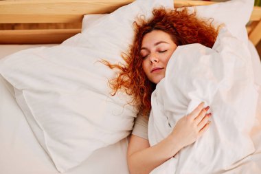 Bir kız çarşaflarla kaplı rahat yatağında uyur..