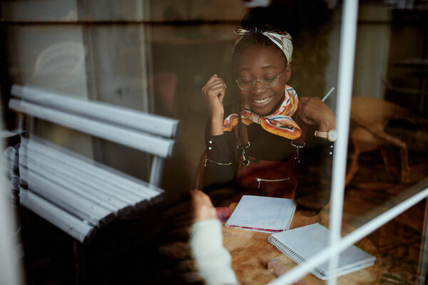 A smiling African college girl sitting in cafe and study for final exam.