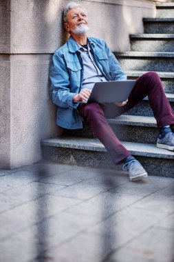 Son sınıf öğrencisi üniversite binasının merdivenlerinde oturur ve sınavdan önce bilgisayarını kullanarak notlara bakar..
