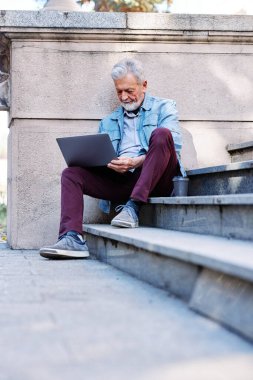 Son sınıf öğrencisi üniversite binasının merdivenlerinde oturur ve sınavdan önce bilgisayarını kullanarak notlara bakar..
