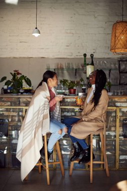 İki çok kültürlü arkadaş kafeteryada oturur, içecek içer ve sohbet ederiz..