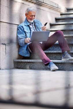Son sınıf öğrencisi üniversite binasının merdivenlerinde oturur ve sınavdan önce bilgisayarını kullanarak notlara bakar..