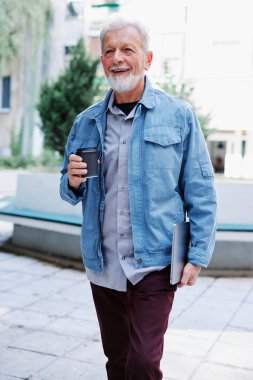 Mutlu bir son sınıf öğrencisi sokakta dizüstü bilgisayarını ve kahve fincanını tutuyor. Son sınıf öğrencisi bir konferansa gidiyor..