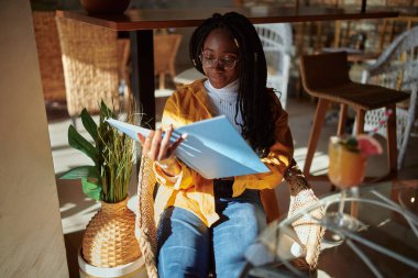 Afrikalı bir üniversiteli kız kampüsteki kafeteryada gelişigüzel oturuyor ve sınava çalışıyor..