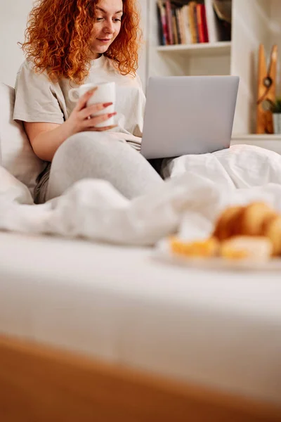 Zencefilli Bir Kız Sabah Yatağında Oturur Sabah Kahvesini Içer Bilgisayarını — Stok fotoğraf