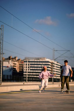 İki genç kaykay yapıyor ve kameraya doğru koşuyor..