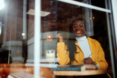 Zeki bir Afrikalı üniversiteli kız kafeteryada oturur ve sınav için çalışır. Fotoğraf dışardan çekilmişti. Öğrenci değişim programında bir kız bir kafede oturuyor ve okuyor..
