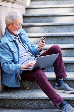 Üniversite binasının önündeki merdivenlerde elinde dizüstü bilgisayarla son sınıf öğrencisi oturuyor. Geri çekilen konsept.