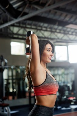 Zayıf bir sporcu kadın spor salonunda dambıllarla antrenman yapıyor..