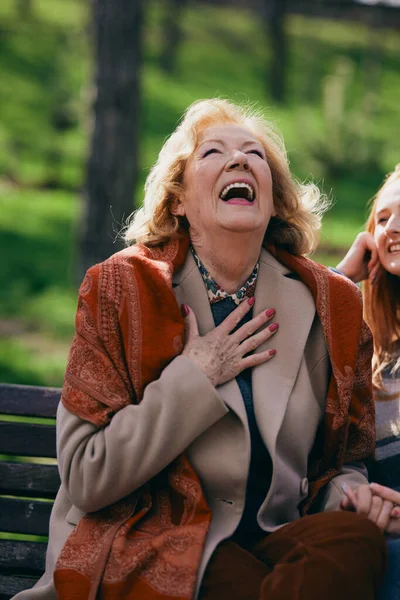 Bir büyükanne parkta bankta otururken ergen torunuyla gülüp eğleniyor..