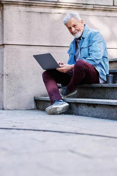 Üniversite binasının önündeki merdivenlerde elinde dizüstü bilgisayarla oturan mutlu bir son sınıf öğrencisi ders çalışıyor. Geri çekilen konsept.