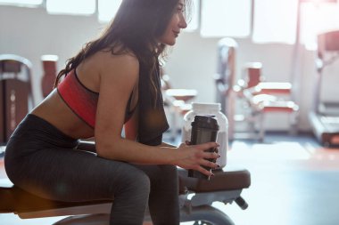 Genç aktif kadın spor salonunda mola veriyor. Omuzlarında havluyla bir su şişesi tutuyor..