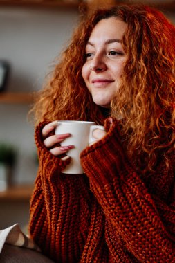 Kızıl kıvırcık saçlı tatlı bir kadın sabahları kahvesinin tadını çıkarıyor..
