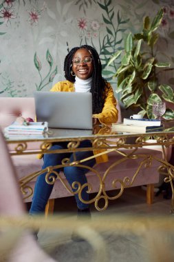 Kafeteryadaki laptopuyla okul ödevini yapan neşeli, genç Afrikalı kadın..