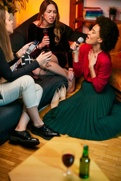 友達のためにカラオケを歌いながらホームパーティーを楽しむ多文化の若い女性2人 — ストック写真