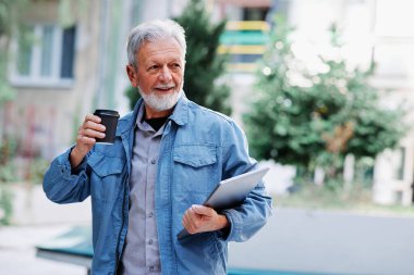 Yeniden eğitim programındaki mutlu bir son sınıf öğrencisi elinde bir laptop ve kahveyle üniversitenin önünde duruyor..