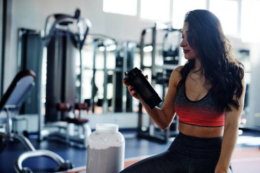 Genç aktif bir kadın protein içeceğiyle spor salonunda mola veriyor..