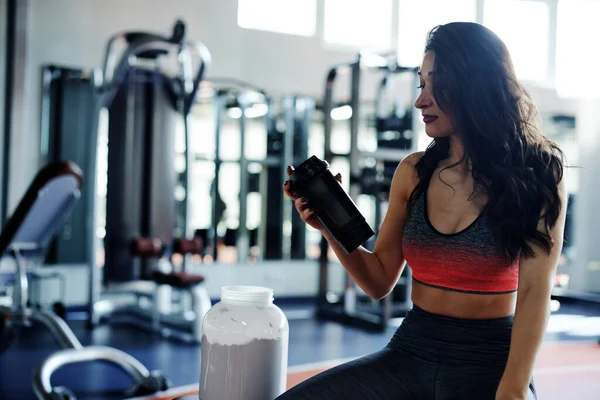 Genç aktif bir kadın protein içeceğiyle spor salonunda mola veriyor..