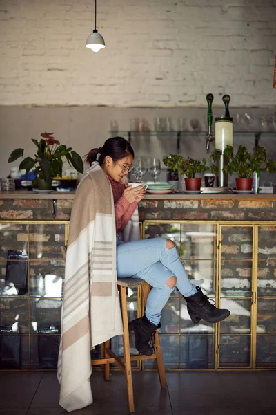 Genç bir Asyalı kadın kafeteryada battaniyesiyle çay içiyor..