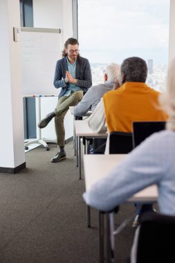 Genç hipster öğretmeni sınıftaki sosyal medya hakkında çok kültürlü bir grup üst düzey insanı eğitiyor..