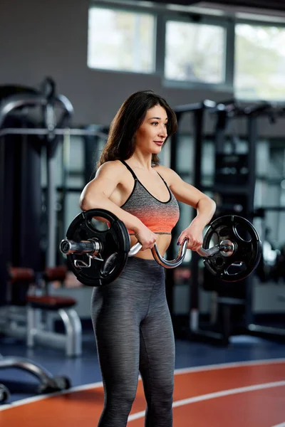 Spor giyim camiasında ağırlık kaldıran genç, formda bir kadın..