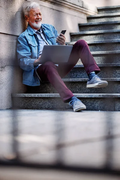 Üst düzey bir iş adamı dışarıda merdivenlerde oturur ve iş için dizüstü bilgisayar kullanır..