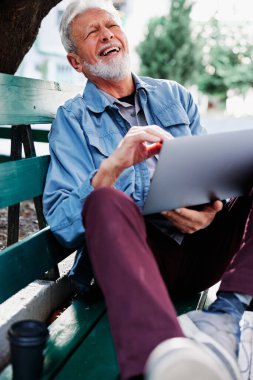 Mutlu bir son sınıf öğrencisi parkta bankta oturur ve dizüstü bilgisayarını kucağında tutar. Eğitimdeki son sınıf öğrencileri.
