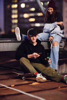 Genç bir kaykaycı çocuk ve kız arkadaşı binanın çatısında oturup bira içerek eğleniyorlar..