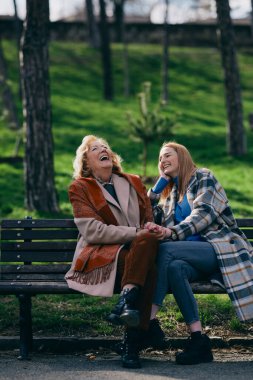 Bir büyükanne parkta bankta otururken ergen torunuyla gülüp eğleniyor..