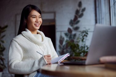 Asyalı bir kız öğrenci bir kafede otururken dizüstü bilgisayarla ödevini yapıyor..