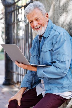 Mutlu bir son sınıf öğrencisi tuğla duvarın önünde dizüstü bilgisayarda yazı yazıyor..