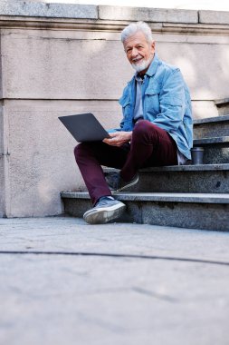 Son sınıf öğrencisi üniversite binasının merdivenlerinde oturur ve sınavdan önce bilgisayarını kullanarak notlara bakar..