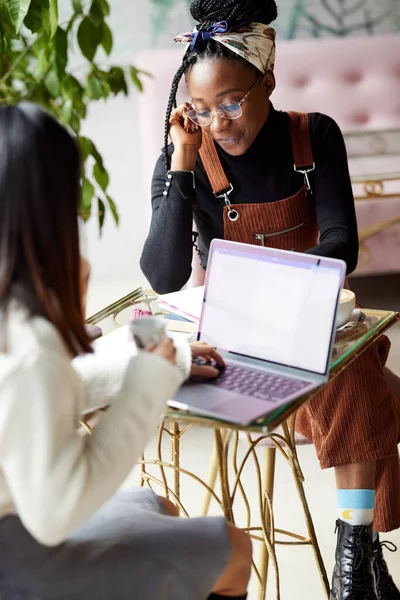 İki çok kültürlü kız öğrenci bir internet kafede otururken dizüstü bilgisayarla bir proje üzerinde çalışıyorlar..