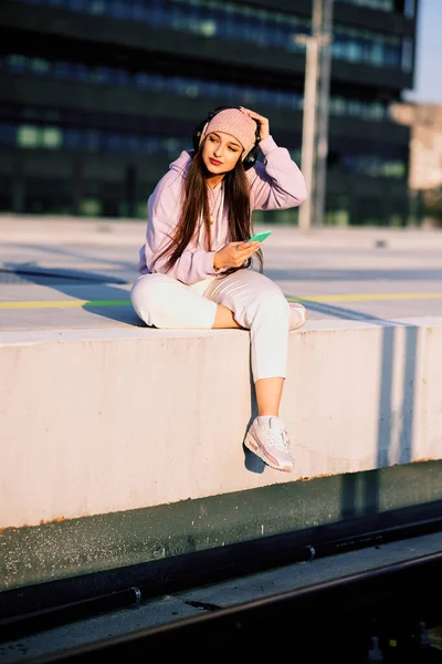 Teenage Girl Urban Wear Sits Railroad Platform Headphones Browses Song — стоковое фото