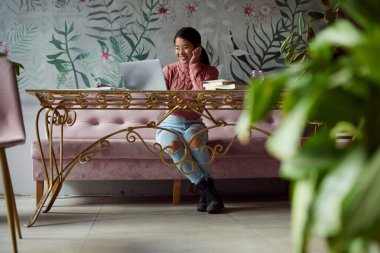 Çok kültürlü bir kız öğrenci, bir kafede bilgisayarını e-öğrenim için kullanıyor..