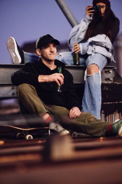 Genç bir kaykaycı çocuk ve kız arkadaşı binanın çatısında oturup bira içerek eğleniyorlar..