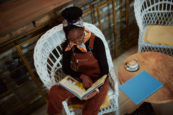 A multicultural girl is reading an encyclopedia in a coffee shop and having fun.