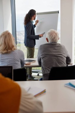 Bir öğretmen tahtaya yazı dersi yazıyor ve son sınıf öğrencilerine tablet tutarken anlatıyor..