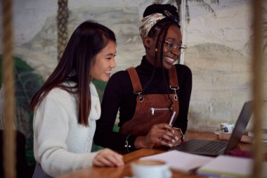 İki çok ırklı kız öğrenci bir barda oturup kitap okuyor. Öğrenciler sınava çalışıyor..