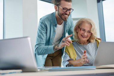 Genç bir hippi öğretmen son sınıf öğrencisine dizüstü bilgisayar kullanmayı öğretiyor..