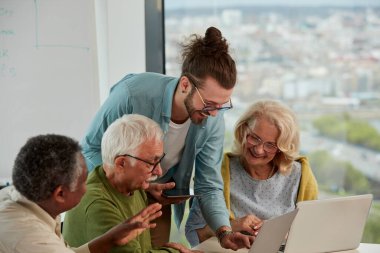 Elinde tablet tutan genç bir eğitimci ve çok kültürlü son sınıf öğrencilerine web tasarımı yapmayı öğretiyor..