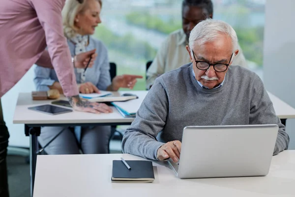 Senior Man Types Laptop Classroom While Young Teacher Showing Other — Stockfoto