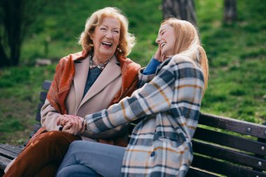 Bir büyükanne parkta bankta otururken ergen torunuyla gülüp eğleniyor..