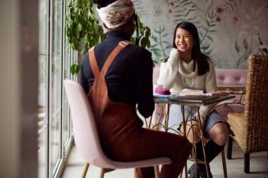 İki çok kültürlü kız öğrenci bir kafede oturup final sınavına çalışıyor..