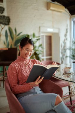 Çok kültürlü bir kız bir kafede kitap okuyor ve eğleniyor..